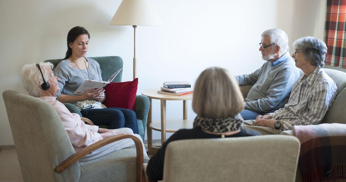 Kvinna läser högt ur en bok för äldre personer 